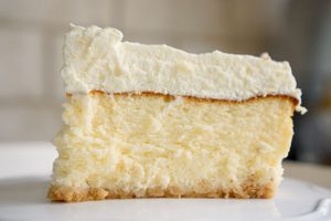 פרוסת עוגת גבינה גבוהה עם קצפת על צלחת פרחונית. מתכון לעוגת גבינה מושלמת לפסח. גבישס - בלוג האוכל של מירב גביש